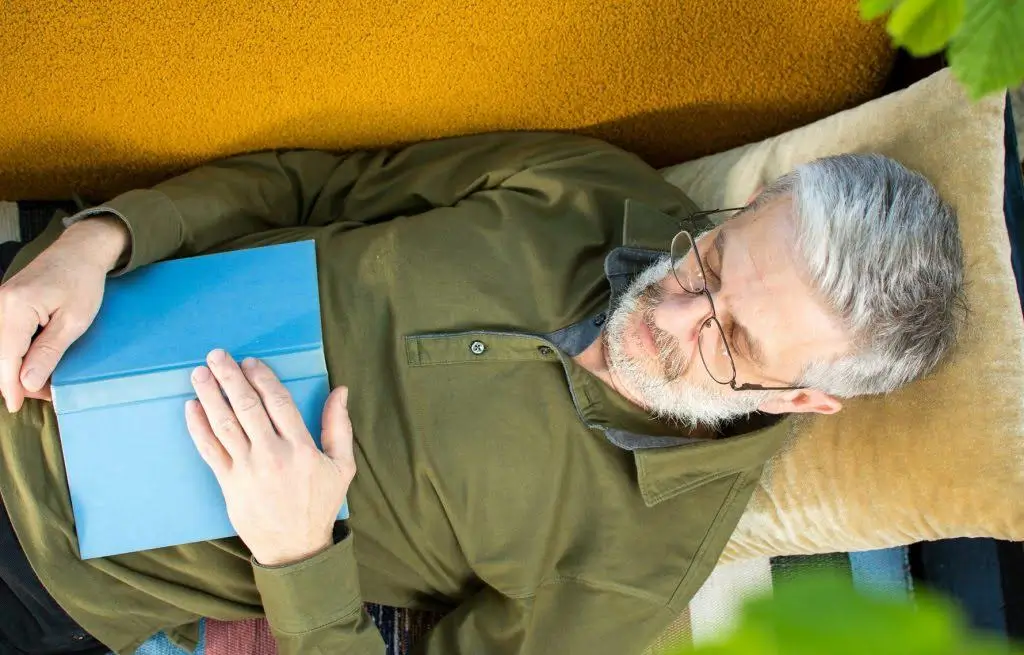 Mies nukkuu sohvalla kirja sylissä